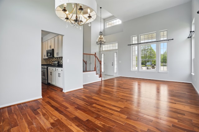 122 Periwinkle Ln, Bolingbrook, IL 60490 - unfurnished living room with a chandelier, a towering ceiling, dark wood-style flooring, stairs, and baseboards
