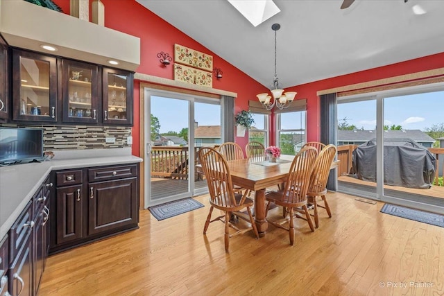 dining area with a skylight, high vaulted ceiling, a chandelier, light wood-style flooring, and healthy amount of natural light