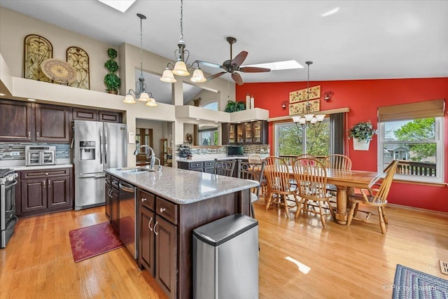 kitchen with a skylight, appliances with stainless steel finishes, a sink, dark brown cabinets, and high vaulted ceiling