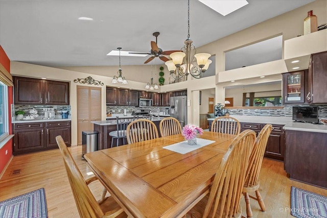 dining area featuring a chandelier, light wood-style flooring, a ceiling fan, and high vaulted ceiling
