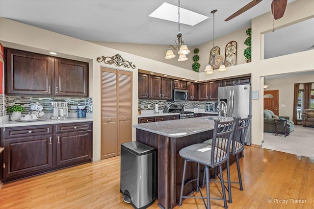 kitchen featuring stainless steel appliances, a skylight, tasteful backsplash, a kitchen bar, and decorative light fixtures