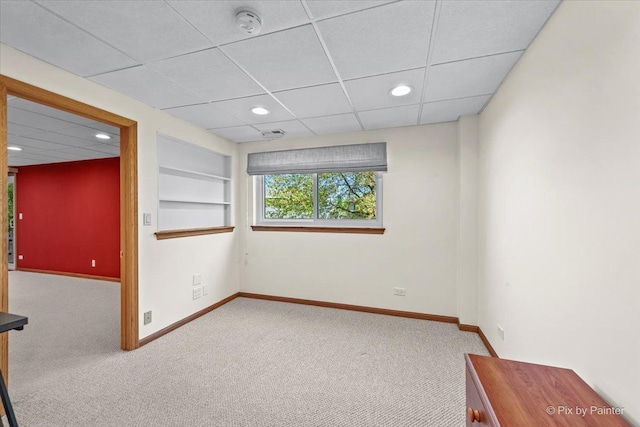 carpeted spare room featuring baseboards, recessed lighting, a paneled ceiling, built in shelves, and a smoke detector