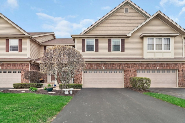 view of property with brick siding, an attached garage, driveway, and a front lawn