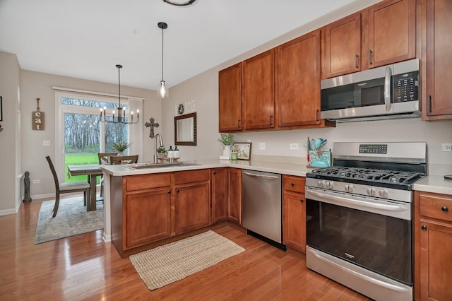 kitchen with brown cabinets, light wood-type flooring, a sink, a peninsula, and stainless steel appliances