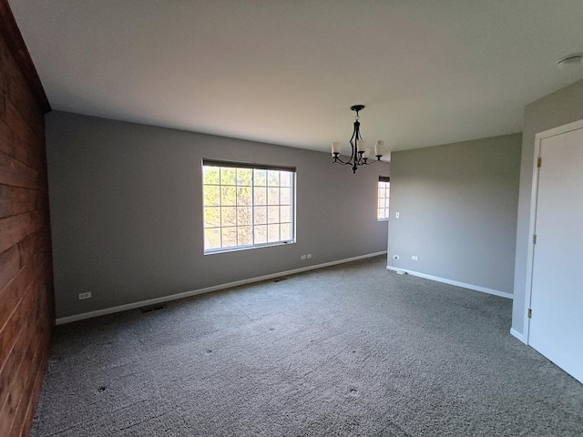 carpeted empty room with a chandelier and baseboards