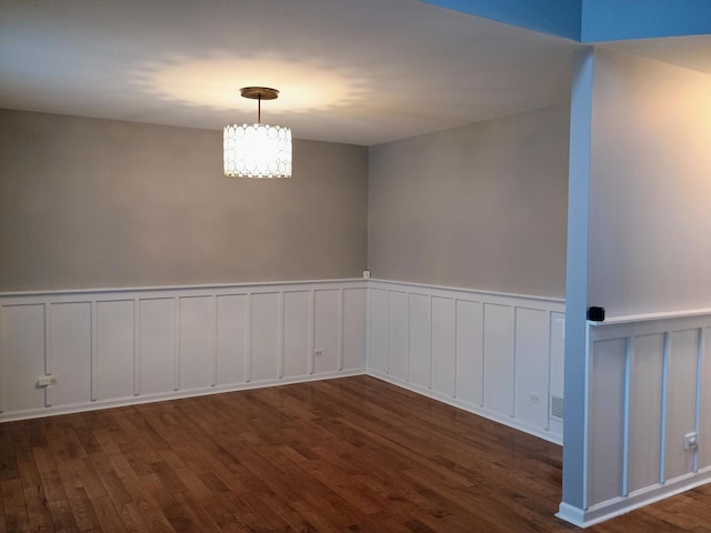 empty room featuring a decorative wall, an inviting chandelier, wainscoting, and wood finished floors