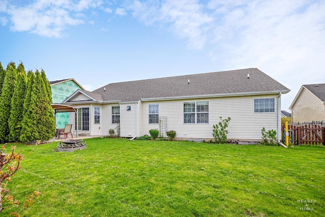 rear view of property with a lawn, fence, a fire pit, and a shingled roof