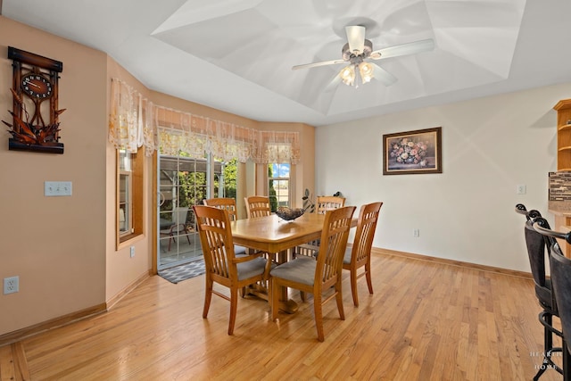 dining area with ceiling fan, a raised ceiling, baseboards, and light wood-style flooring