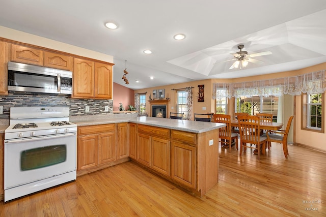 kitchen with a glass covered fireplace, stainless steel microwave, light wood-type flooring, tasteful backsplash, and white range with gas cooktop