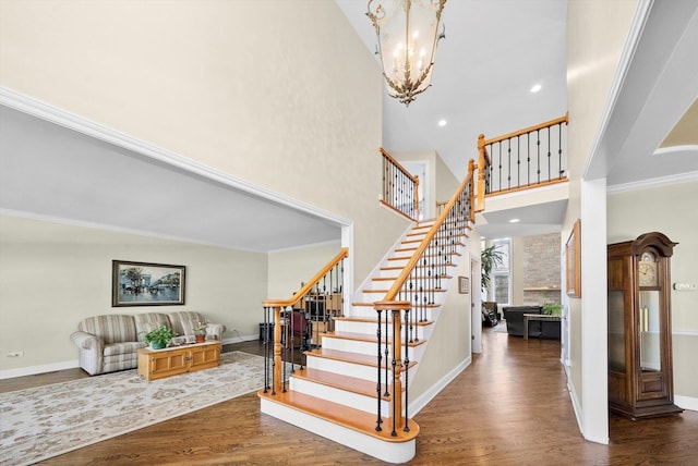 stairway with crown molding, a chandelier, baseboards, wood finished floors, and a high ceiling