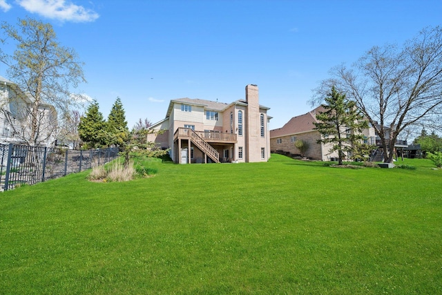 rear view of house featuring a chimney, a deck, a yard, stairway, and fence
