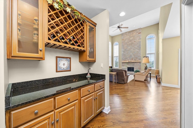 bar featuring recessed lighting, wood finished floors, ceiling fan, a stone fireplace, and a dry bar