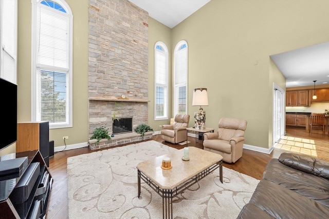 living room with a fireplace, wood finished floors, baseboards, and a high ceiling