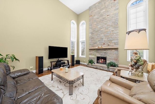 living room featuring baseboards, high vaulted ceiling, wood finished floors, and a fireplace
