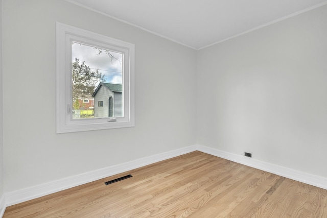 empty room with baseboards, visible vents, ornamental molding, and light wood-style floors