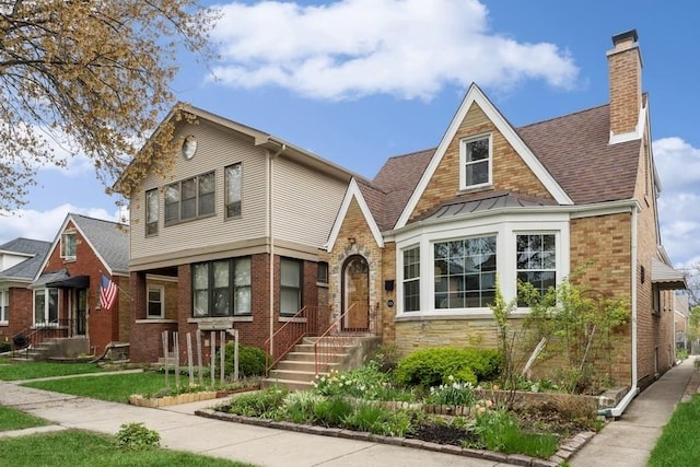 tudor home featuring a shingled roof, a chimney, a standing seam roof, and brick siding