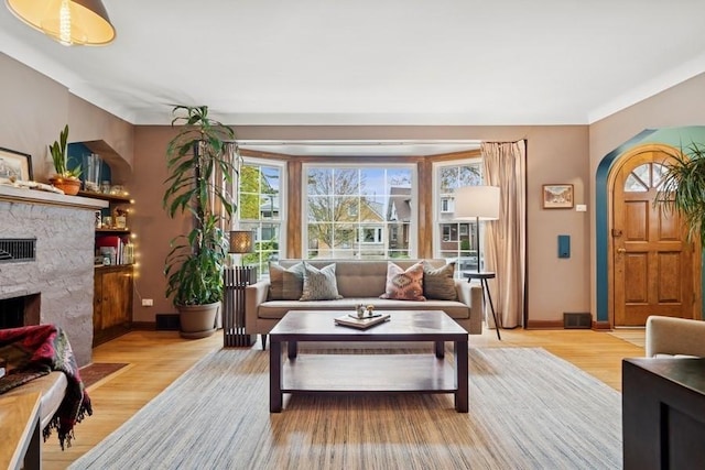 living room featuring a fireplace with flush hearth, baseboards, light wood-type flooring, and arched walkways