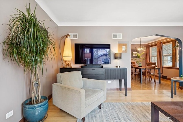living room featuring arched walkways, baseboards, light wood-style flooring, and visible vents