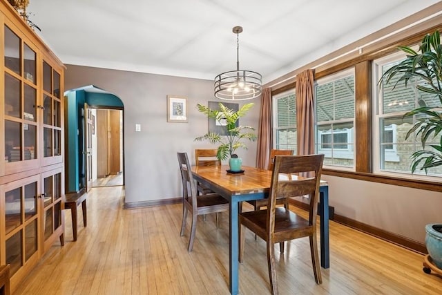 dining room featuring baseboards, arched walkways, a notable chandelier, and light wood-type flooring