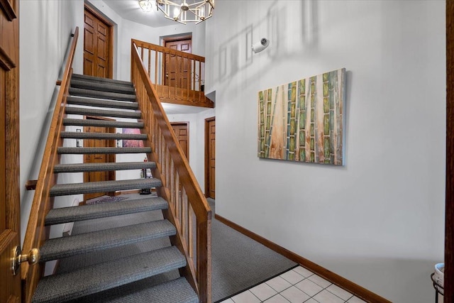 staircase featuring carpet floors, a chandelier, tile patterned floors, and baseboards