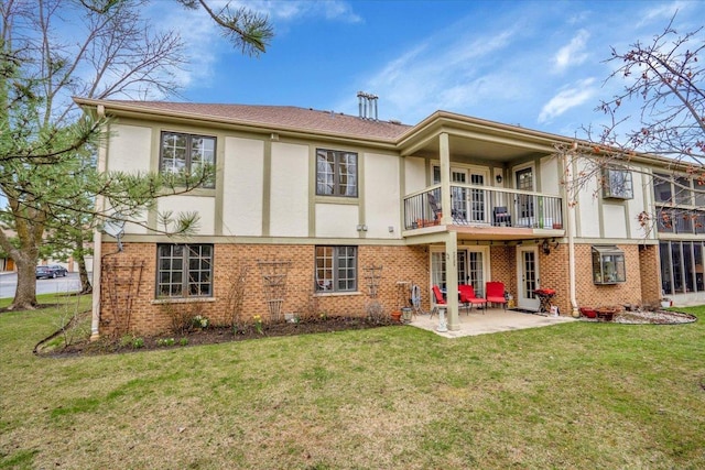rear view of house featuring a balcony, a patio, a lawn, stucco siding, and brick siding