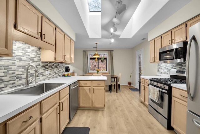 kitchen with a sink, light brown cabinets, a peninsula, a skylight, and appliances with stainless steel finishes
