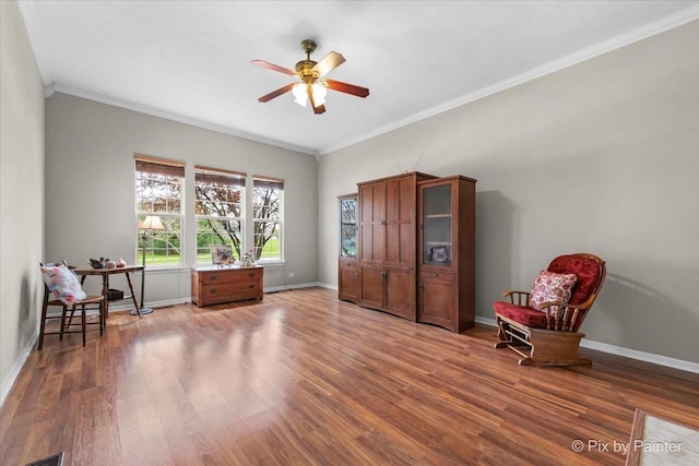 sitting room with crown molding, a ceiling fan, baseboards, and wood finished floors