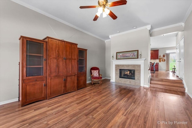 living room with a tiled fireplace, ornamental molding, a ceiling fan, and wood finished floors