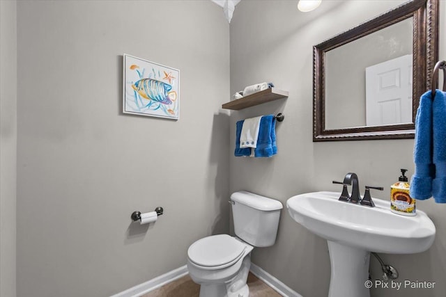 half bath with baseboards, a sink, tile patterned flooring, and toilet