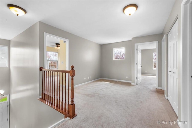 hall featuring carpet flooring, baseboards, an upstairs landing, and a healthy amount of sunlight