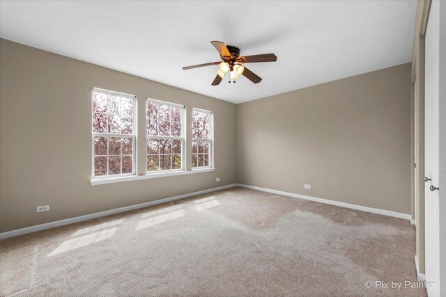 carpeted spare room featuring baseboards, a ceiling fan, and visible vents