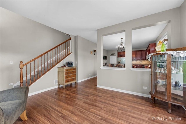 living room featuring stairway, baseboards, wood finished floors, and a notable chandelier