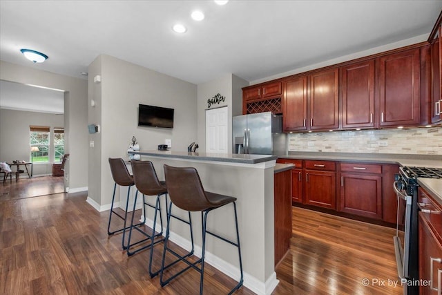 kitchen with decorative backsplash, a breakfast bar, dark brown cabinets, dark wood-style floors, and stainless steel appliances