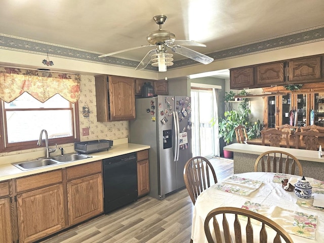 kitchen featuring stainless steel fridge, black dishwasher, light countertops, light wood finished floors, and a sink
