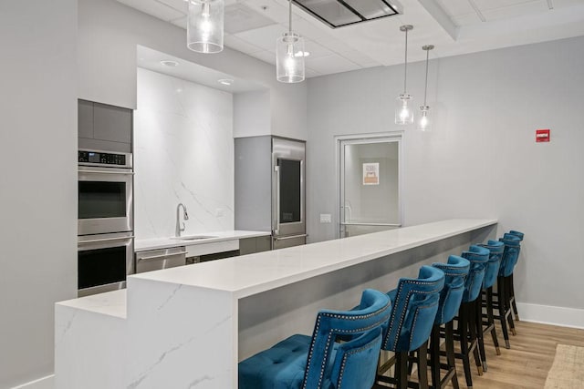 kitchen with pendant lighting, a sink, appliances with stainless steel finishes, light wood-style floors, and modern cabinets