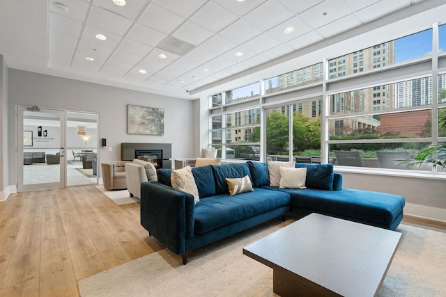 living area featuring a drop ceiling, a glass covered fireplace, light wood-style floors, and baseboards