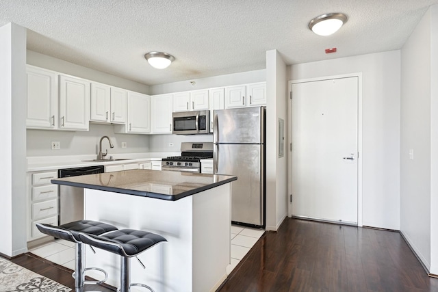 kitchen featuring a sink, a breakfast bar, white cabinetry, appliances with stainless steel finishes, and wood finished floors