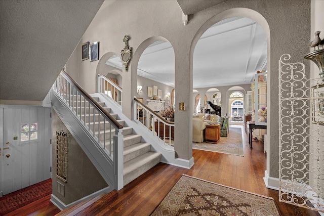 foyer entrance with wood finished floors, arched walkways, stairway, and ornamental molding