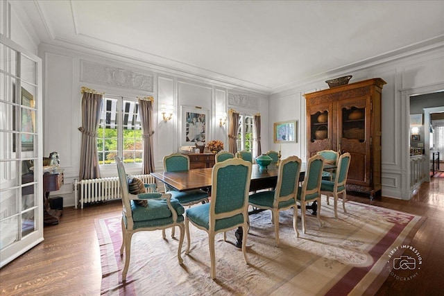 dining room with a decorative wall, radiator heating unit, wood finished floors, ornamental molding, and healthy amount of natural light