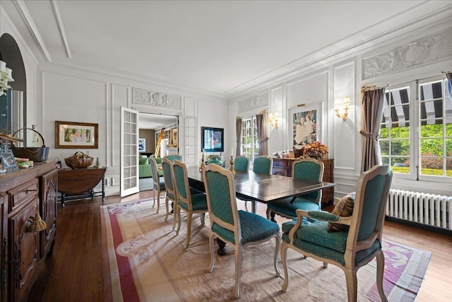 dining room with a decorative wall, radiator, wood finished floors, crown molding, and plenty of natural light