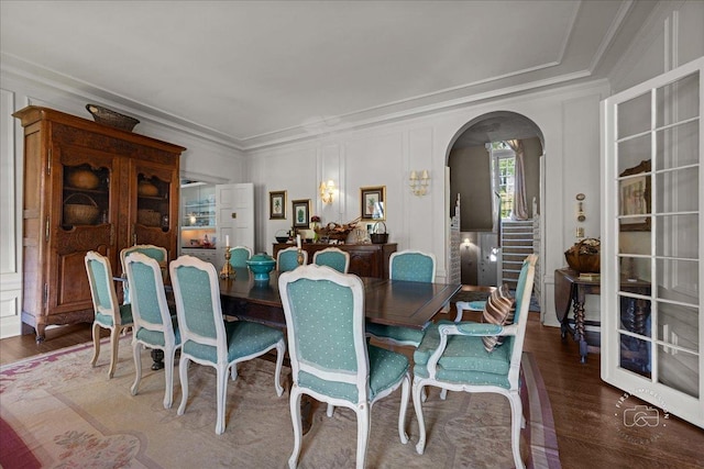 dining room featuring arched walkways, ornamental molding, wood finished floors, and a decorative wall