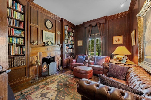 living area featuring dark wood-style flooring, built in shelves, a fireplace with flush hearth, wooden walls, and ornamental molding