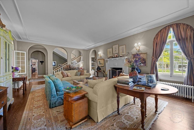 living room with radiator heating unit, wood finished floors, arched walkways, a fireplace, and ornamental molding