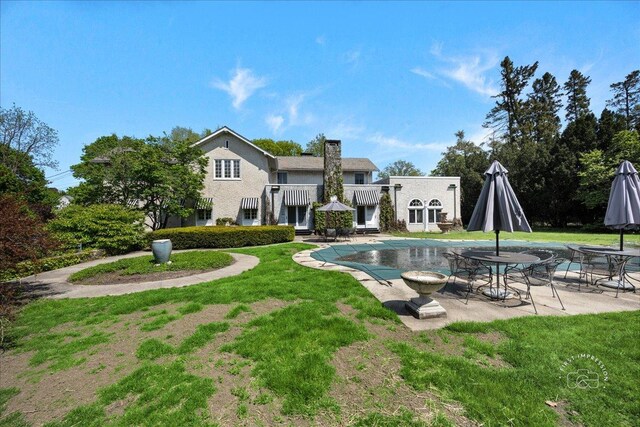 rear view of house with a patio, a yard, a covered pool, and a chimney
