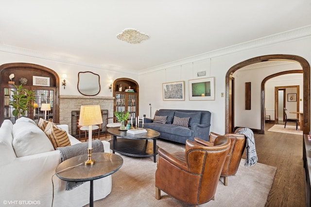 living room featuring arched walkways, ornamental molding, wood finished floors, and a fireplace
