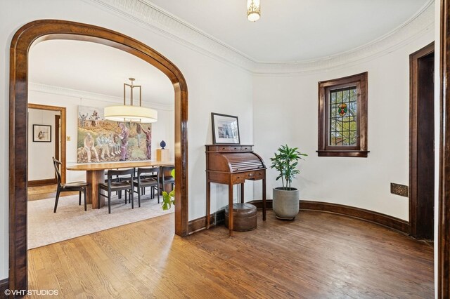 corridor featuring arched walkways, ornamental molding, and wood finished floors
