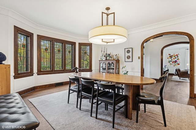 dining space with arched walkways, wood finished floors, and plenty of natural light