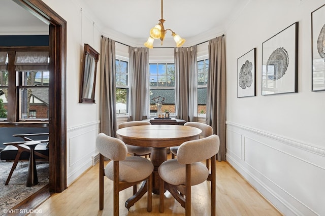 dining area with a decorative wall, a wainscoted wall, light wood-style flooring, and a chandelier
