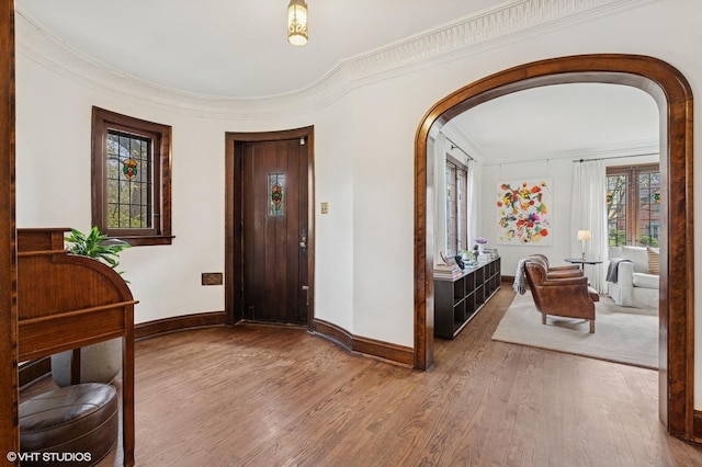 foyer entrance with baseboards, arched walkways, and wood finished floors