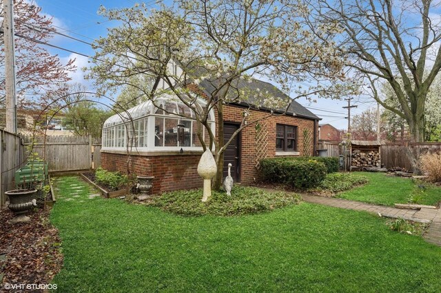 view of side of property featuring brick siding, a fenced backyard, a vegetable garden, and a yard